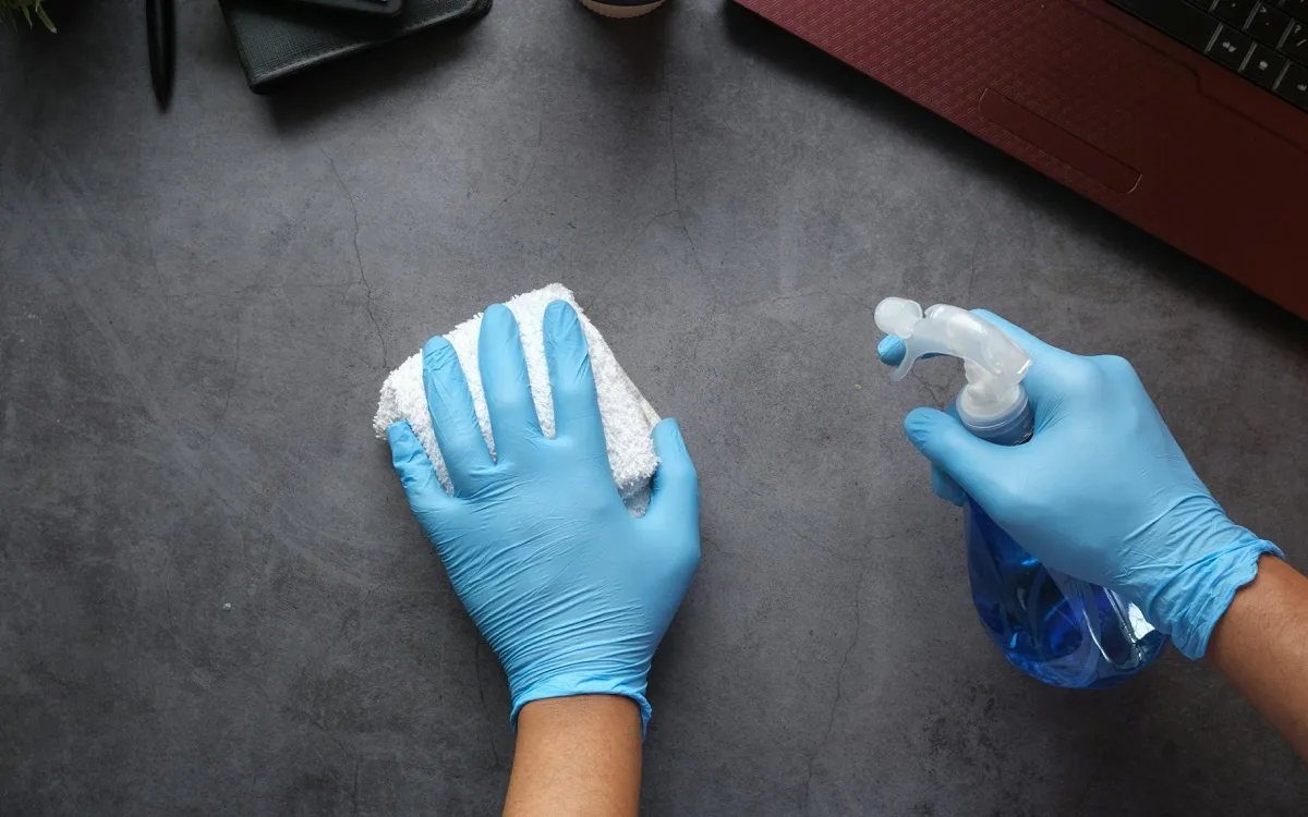 Sanificazione di una scrivania da ufficio con guanti e detergente spray